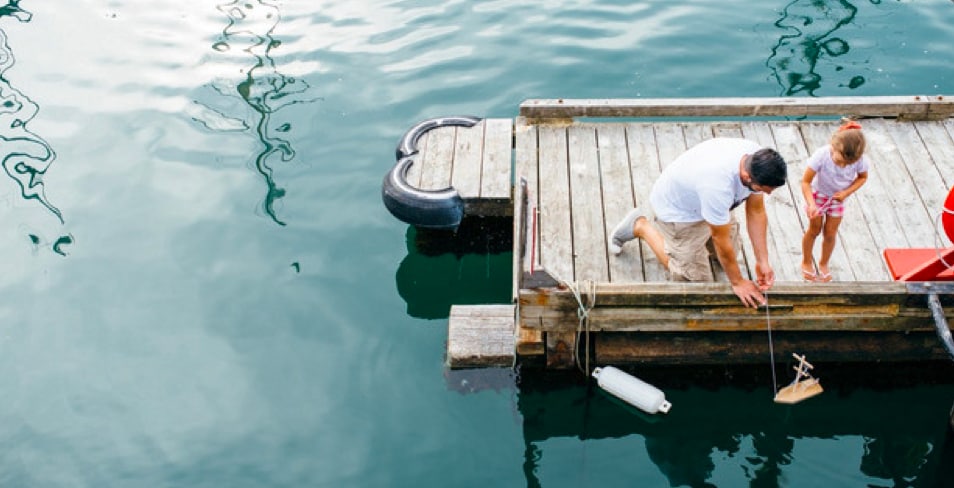 Father and daughter playing with a toy boat off a dock
