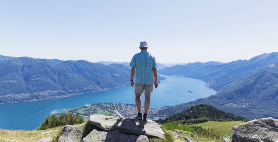 Older man standing at the top of a mountain looking off into valley with river