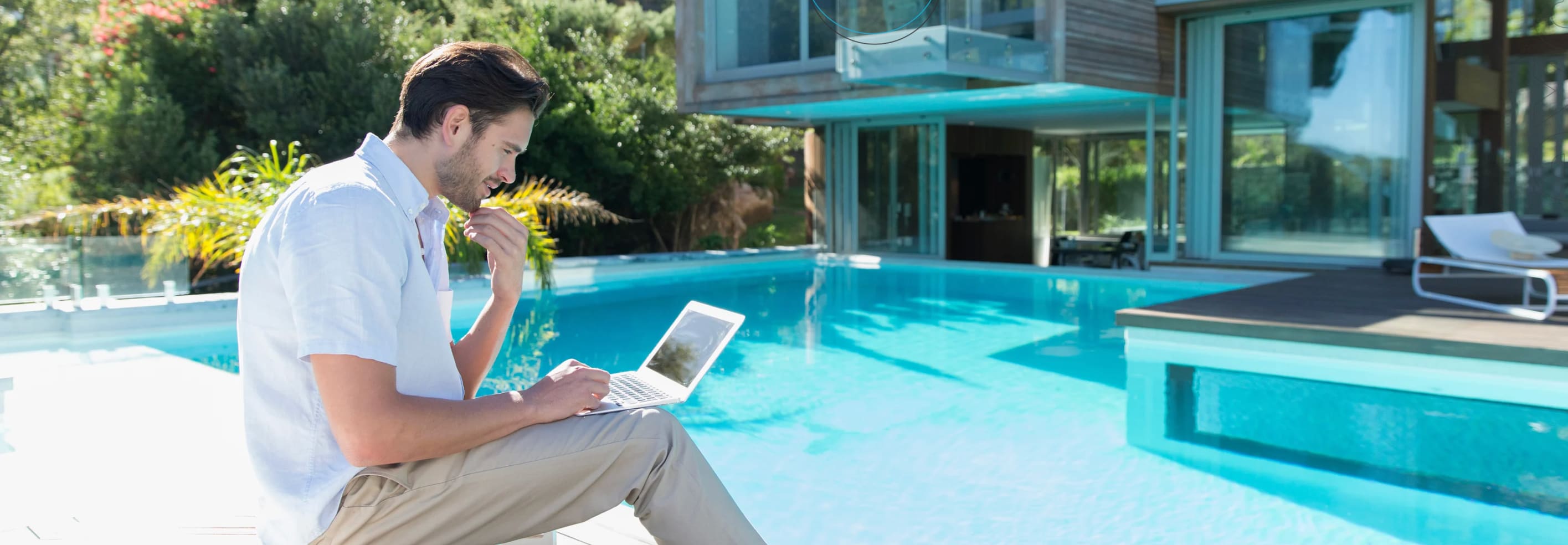 Photo of male in short sleeve top sitting by the pool with a laptop on his lap